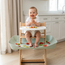 Baby in a wooden high chair using the food catcher at mealtime