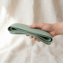 Sage-green food catcher folded flat, held in one hand for travel